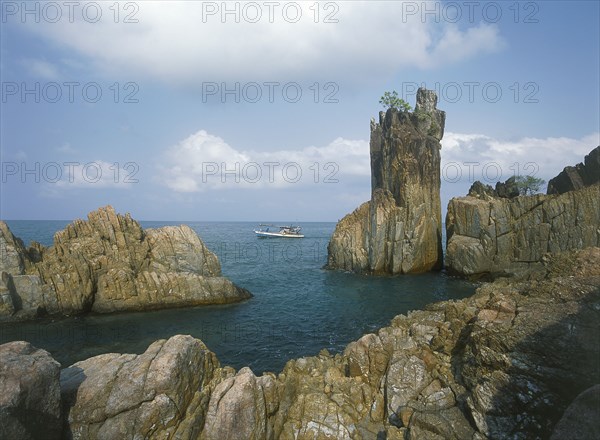 THAILAND, Trat Province, Koh Chang, Laem Chai Chet. Coastal rock formations and cliffs with a small boat  passing by.