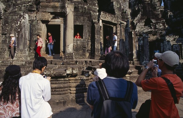 CAMBODIA, Siem Reap Province, Angkor Thom, The Bayon.  Tourists posing for photographs amongst the temple architecture.