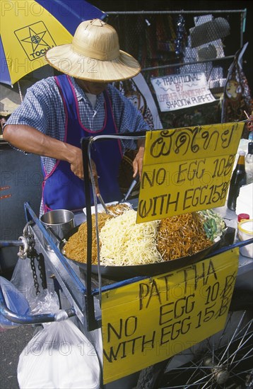 THAILAND, Bangkok, Khao San Road. Pad Thai food street stall with price signs and man preparing food behind counter.
