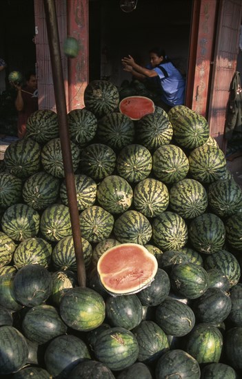 THAILAND, North, Chiang Mai, "Wholesale Food Market.  Large pile of watermelon for sale, woman with arms raised in doorway behind. "