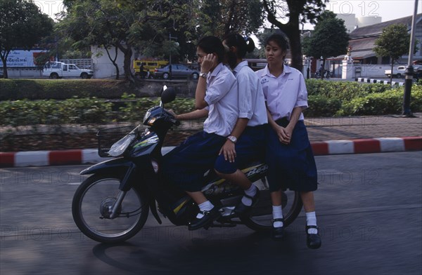 THAILAND, North, Chiang Mai, Speeding moped carrying three girls dressed in uniform with the driver talking on a mobile phone.