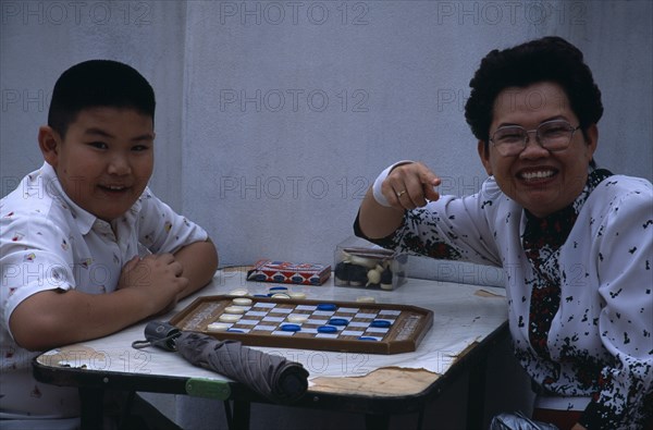 THAILAND, North, Chiang Mai , "Woman and young boy playing drafts, turned to camera smiling and pointing."