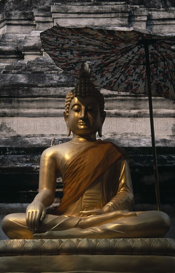 THAILAND, North, Chiang Mai, Wat Bupparam Temple on Tha Phae Road. Seated Golden Buddha statue shaded by large umbrella.
