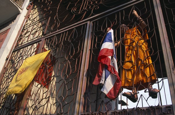 THAILAND, North, Chiang Mai, Wat Saen Fang.  Metalwork partition with monk climbing inside to attach flags.