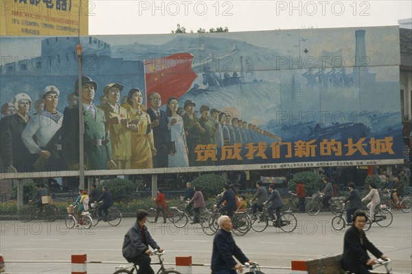 CHINA, Sichuan, Chengdu, ‘Building our new Great Wall’ poster on hoarding beside road with cyclists passing.