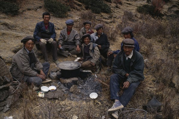 CHINA, Tibet, Terdrom, "Group of labourers having lunch, sitting on ground around cooking pot supported by stones over fire. "