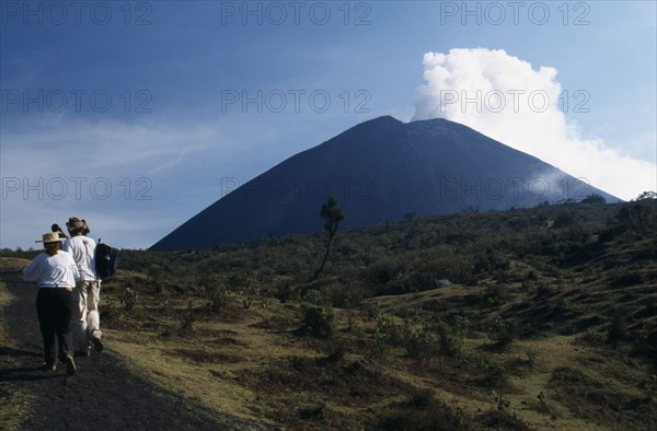 GUATEMALA, Pacaya Volcano, Smoking cone of volcano with people walking a dirt path in the foreground.