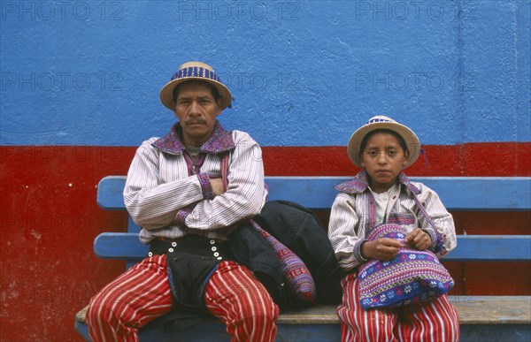 GUATEMALA, Todos Santos Cuchumatan, "Father and Son dressed identically, sitting on a blue bench against a blue and red wall."
