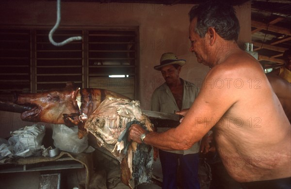 CUBA, Holguin, Palma Soriano, Man carving barbequed pig