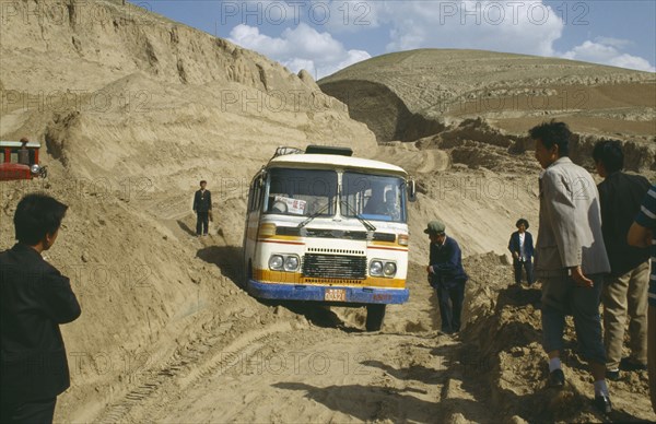 CHINA, Shaanxi , Bus stuck in earth along the main road with people standing by the sides of the dirt track