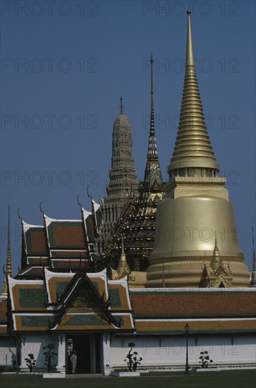 THAILAND, Bangkok, Grand Palace, Aka Wat Phra Kaeo. Exterior view of golden spires and man on guard at the entrance