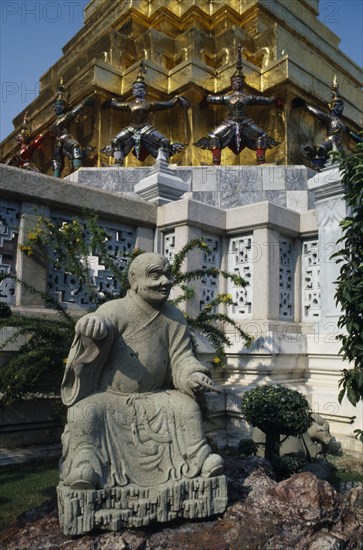 THAILAND, Bangkok, Grand Palace, Aka Wat Phra Kaeo. Stone statue on rockery next to small tree in grounds