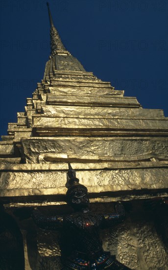 THAILAND, Bangkok, Grand Palace, Wat Phra Kaew. Looking up to detail of statue standing under golden spire