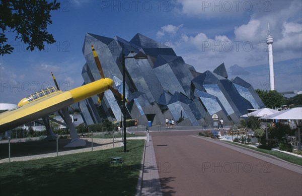 FRANCE, Poitiers, Planet Futuroscope, Le Parc Europeen de l’Image. Sur les traces du Pamda. Path leading to mirrored modern architecture with yellow aircraft in the foreground