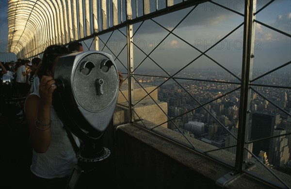 USA, New York , New York City, Woman looking through a chrome viewer at the top of the Empire State Building with views of the city rooftops beyond