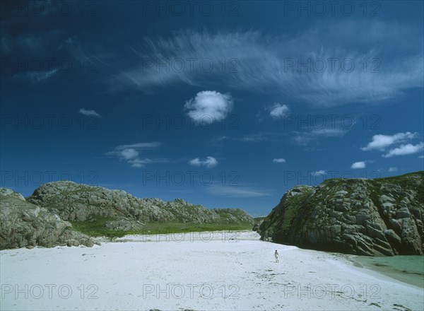 SCOTLAND, Strathclyde, Isle of Mull, White Sand Beach with large moss covered bolders and a woman standing in the distance