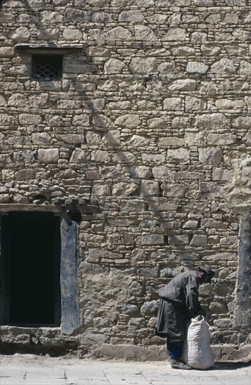 CHINA, Tibet, Lhasa, Man tying sack in the street beside a stone building