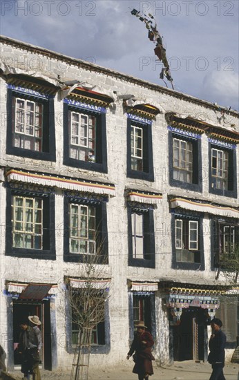 CHINA, Tibet, Lhasa, Traditional houses with ribbons hanging above the windows and people walking in the foreground