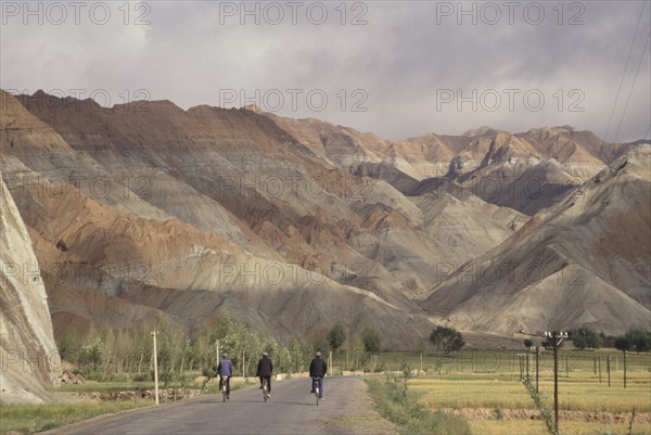 CHINA, Quinghai Province, Near Guide, Row of three cyclists on a road leading toward rocky mountain landscape