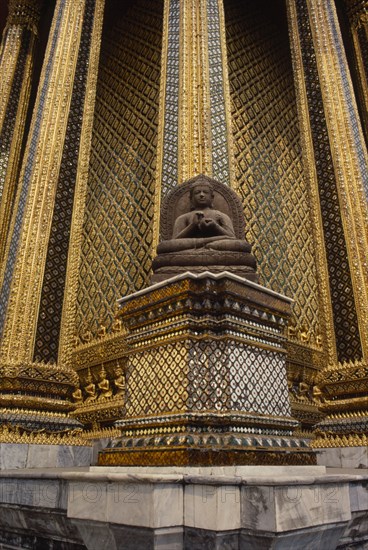 THAILAND, Bangkok, Wat Phra Kaew, Or Grand Palace. Seated buddha statue sitting against golden exterior wall