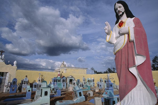 MEXICO, Yucatan, Hoctun, Cemetery with painted religious statue in the foreground and graves painted blue and turquoise behind.