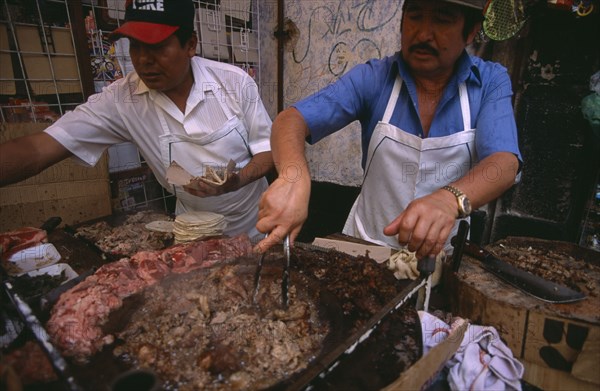 MEXICO, Mexico City, Men cooking meat for tacos and enchiladas on circular hot plate at roadside stall.