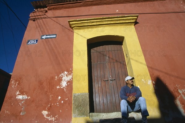 MEXICO, Oaxaca, Oaxaca City, Man in baseball hat sitting on stone step of doorway framed by yellow arch set in red painted wall.