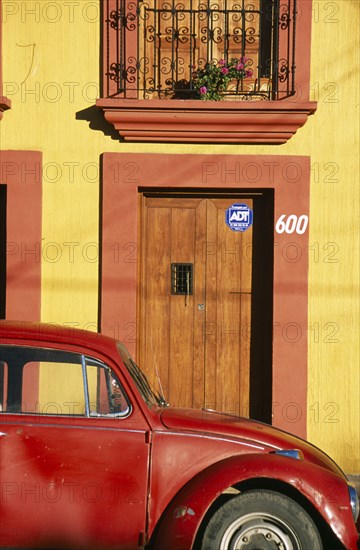 MEXICO, Oaxaca, Oxaca City, Partly seen red volkswagon beetle outside yellow building with wooden door and window shutters in orange painted frames.