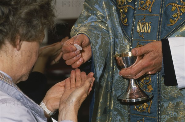 ENGLAND, Religion, Anglican, Woman holding out cupped hands to receive the host from priest during Anglican service.  Cropped view.