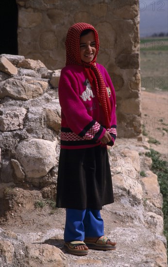 IRAN, Zagros Mountains, Qashqai nomad young girl in red and white spotted headscarf.  Standing with hands clasped in front of her.