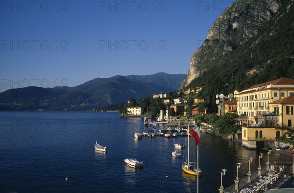 ITALY, Lombardy, Lake Como, Waterfront buildings overlooking moored boats with mountain landscape behind.