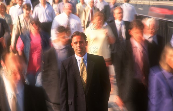 BUSINESS, Commuters, City businessman in suit standing motionless surrounded by crowds in blurred movement.