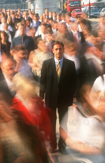 BUSINESS, Commuters, City businessman in suit standing motionless surrounded by crowds in blurred movement.