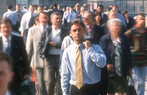 BUSINESS, Commuters, City businessman in shirt and tie holding suit jacket over his shoulder standing motionless surrounded by crowds in blurred movement.