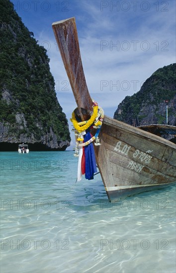 THAILAND, Krabi Province, Ko Phi Phi Leh , Maya Bay.  Close view of prow of long tail boat draped with flower garlands.  Limestone rocks behind.