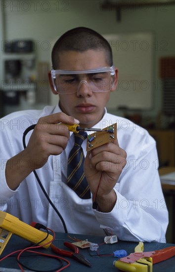 EDUCATION, Secondary School, Science, Schoolboy in electronics class wearing protective glasses during practical experiment.