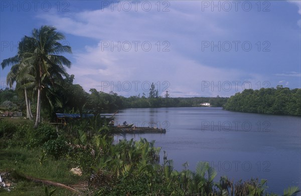 BRUNEI, Brunei River, View along broad stretch of river lined by jungle with man working on boat moored beside small jetty.