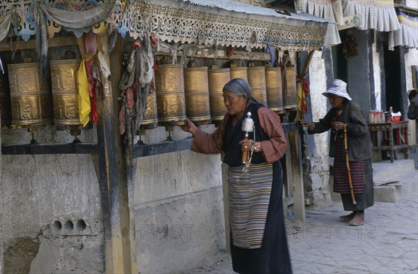 CHINA, Tibet, Shigatse, Two elderly women spinning row of prayer wheels in the street