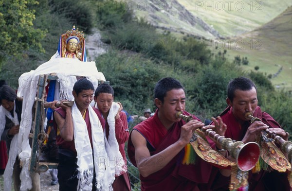 CHINA, Tibet, Lhasa, Drak Yerpa Monastery complex. New statue being carried up to the monastery by monks led by trumpet blowers.