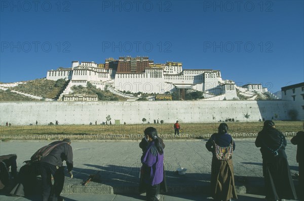 CHINA, Tibet, Lhasa, Potala Palace on the hillside with row of pilgrims prostrating themselves in the foreground.