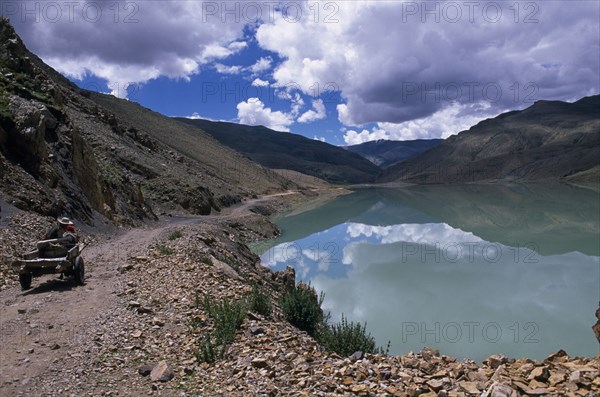 CHINA, Tibet, Shigatse, Man-made dam with horse drawn cart on dusty road running alongside.