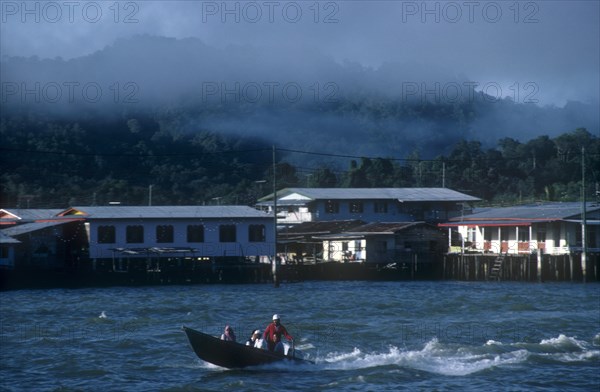 BRUNEI, Bandar Seri Begawan, Morning mist rising from the jungle behind the kampong stilt house village with a water taxi on the river in the foreground
