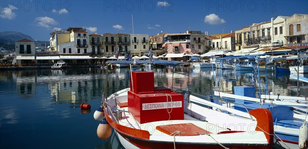 GREECE, Crete, Rethymno, "Venetian Port.  Colourful red, white and blue painted boats moored in harbour overlooked by hotels, bars and restaurants."