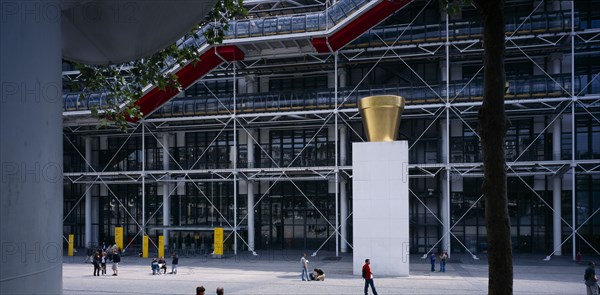 FRANCE, Ile de France, Paris, Pompidou Centre. Exterior of building by Renzo Piano and Richard Rogers. Sculpture and people in plaza area in front of entrance.