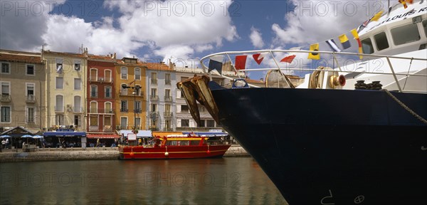 FRANCE, Languedoc-Roussillon, Herault, Sete.  Part view of harbour and colourful waterside buildings with prow of boat draped with flags in the foreground.