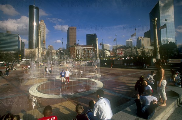 USA, Georgia, Atlanta, "Centennial Olympic Park.  Visitors around paved area with fountains, city skyline behind."