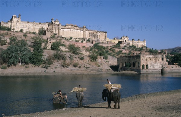 INDIA, Rajasthan, Amber , "Hilltop Palace dating from 1592, seen over water with three elephants and riders in the foreground"