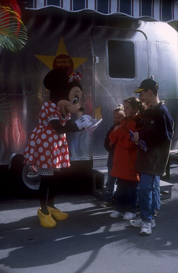 USA, Florida, Orlando, Walt Disney World. Minnie Mouse signing autographs for three children outside her star trailer.