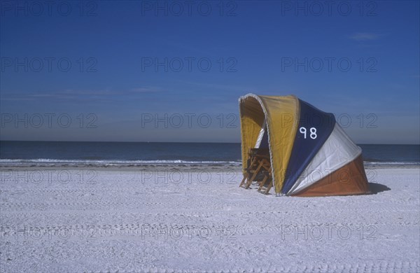 USA, Florida, Clearwater, Clearwater beach with two empty deckchairs shielded by a brightly coloured windbreak.