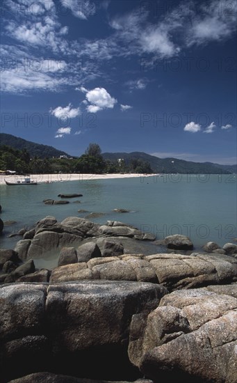 MALAYSIA, Penang, Batu Ferringhi, View over rocks and bay of turquoise water towards distant moored boat and quiet sandy beach.